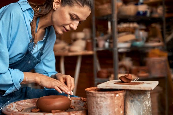 A brunette woman working with clay to make a ceramic bowl. Smoothing the surface of her bowl carefully.