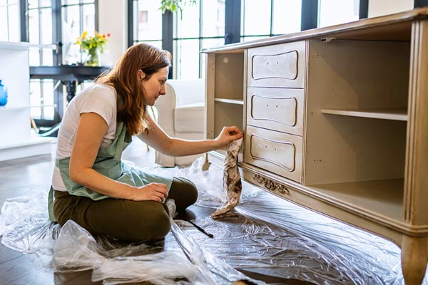A woman is sitting on the floor restoring a large sideboard piece of furniture.
