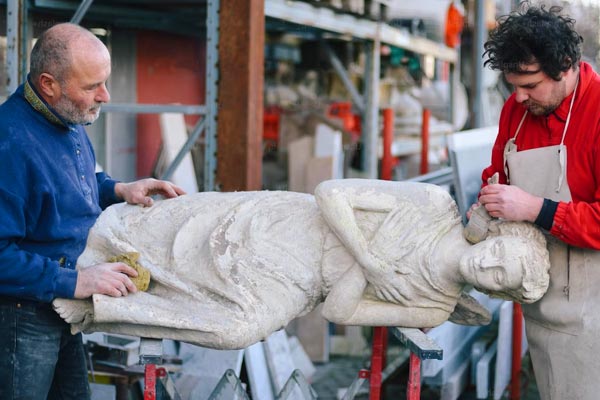 Two men are restoring a marble statue that is laying on its side.