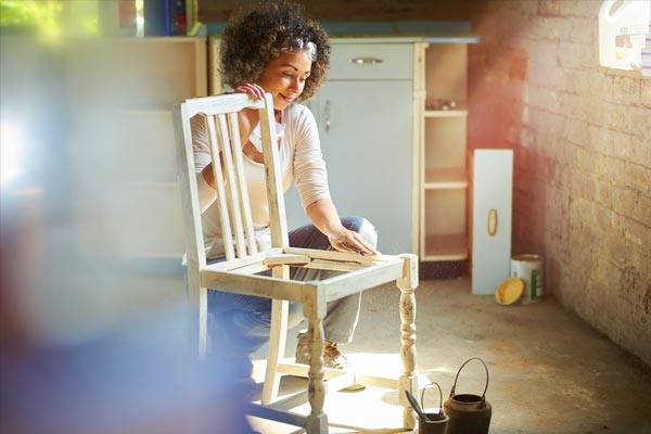 A woman sanding a dining room chair, getting ready to upcyle it.